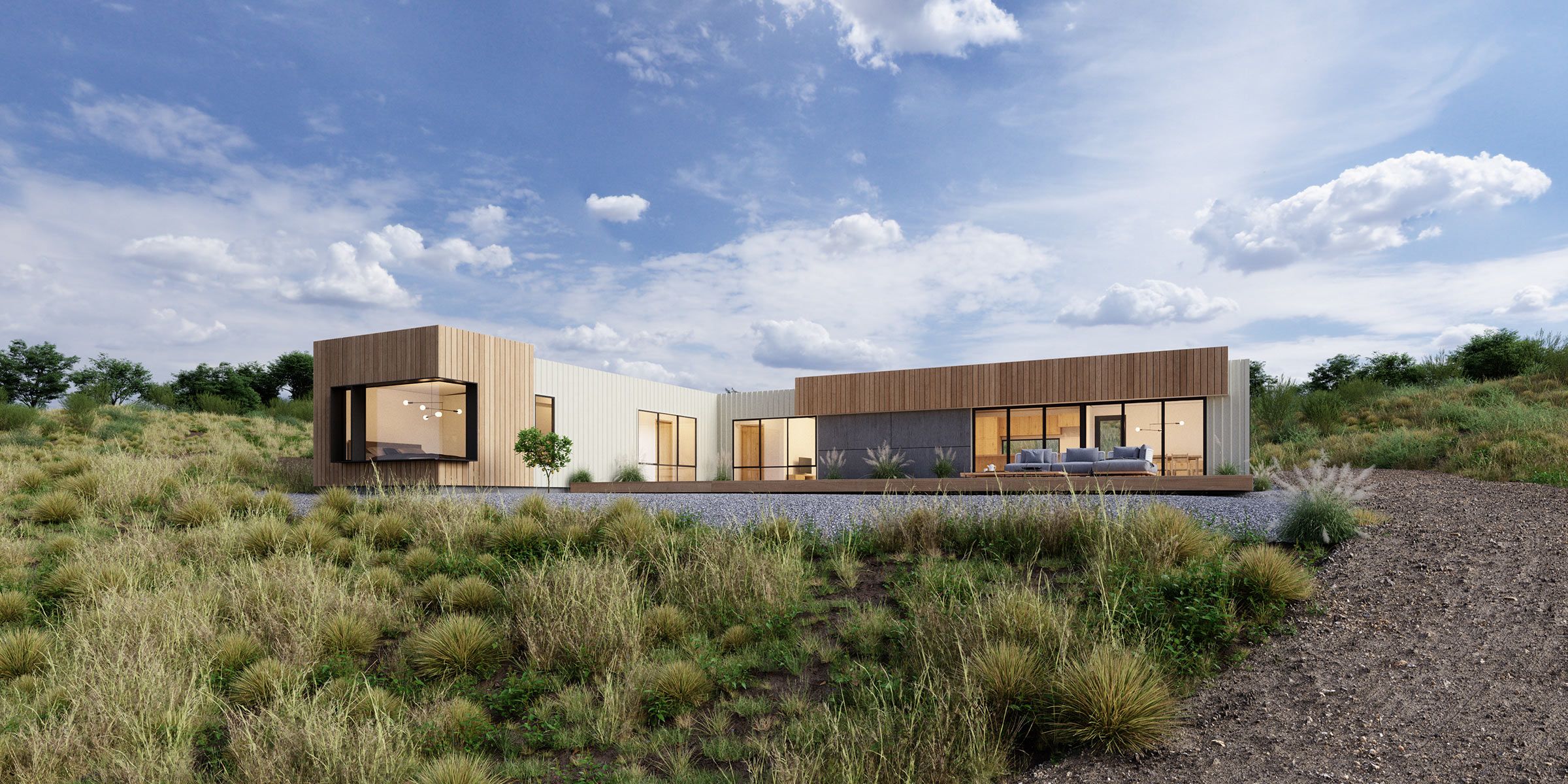 Wide view of a modern single-storey home with timber and light cladding, large floor-to-ceiling windows, and an outdoor deck, set in a grassy, natural landscape under a blue sky with scattered clouds.