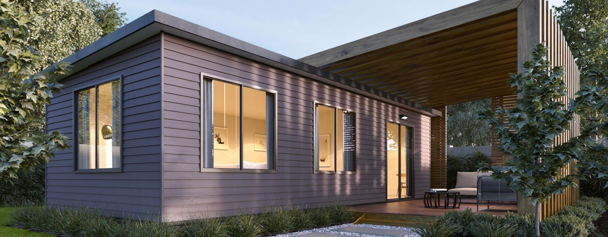 Modern single-storey modular home with dark exterior cladding, large windows, and a covered outdoor patio surrounded by garden greenery.